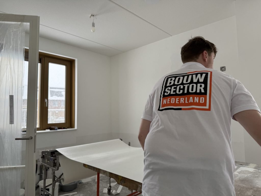 Behanger van Bouwsector Nederland bij de plaktafel met een baan vlies in een lege kame