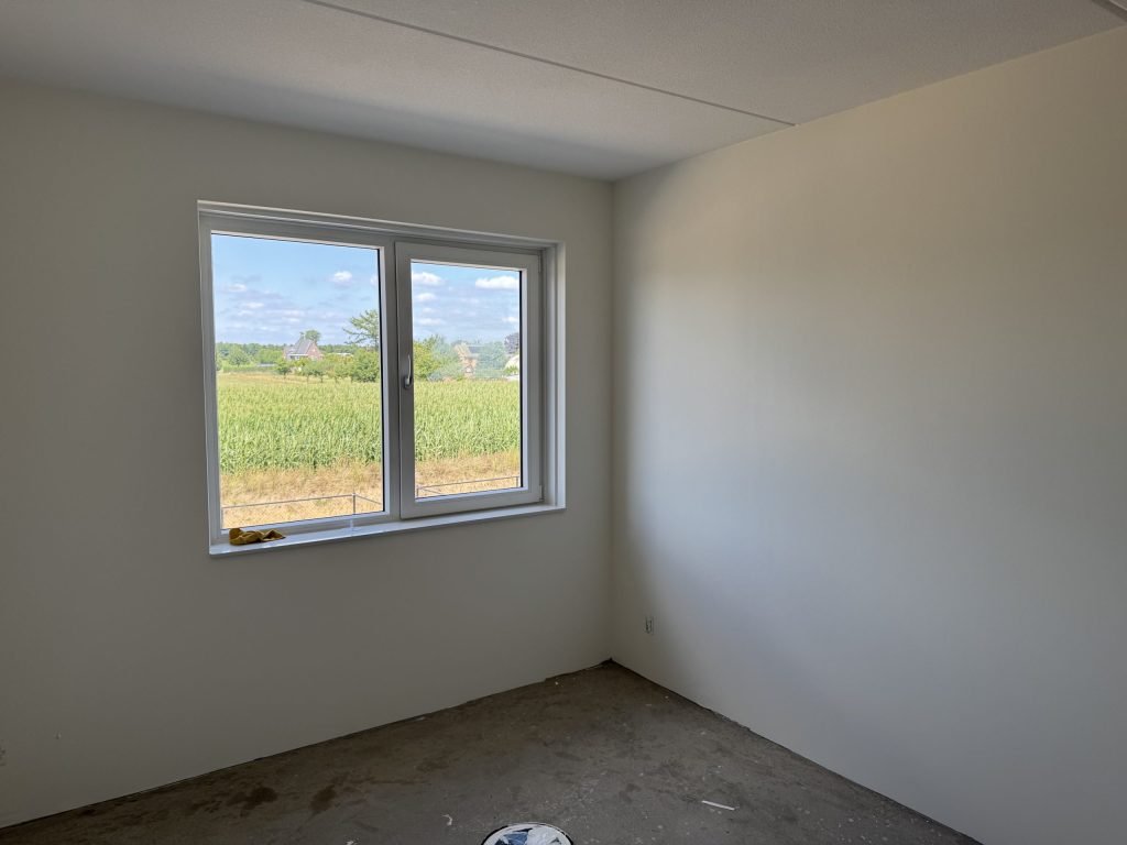Kale, lichte wand naast een raam in een lege kamer, klaar voor de volgende afwerking