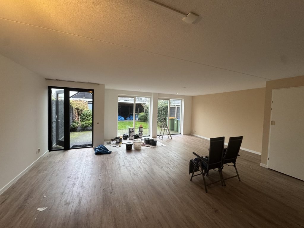 Ruime woonkamer met lichte wanden, tuindeuren en materiaal van de vakmensen op de vloe